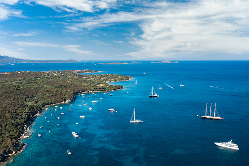 View from above, stunning aerial view of a green coastline with boats and luxury yachts sailing on a turquoise water. Porto Rotondo, Sardinia, Italy.