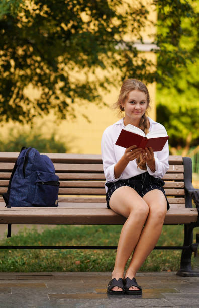 istock Caucasian blond female university, college student sitting on a bench  and reading a book. Back to school, university, college, campus concept. 1337373437