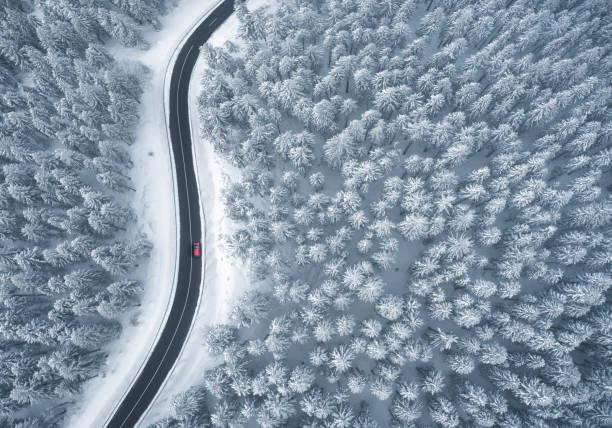 Driving In Snowcapped Forest Red car driving on black asphalt road leading through snowcapped winter forest. Aerial view. winding road photos stock pictures, royalty-free photos & images