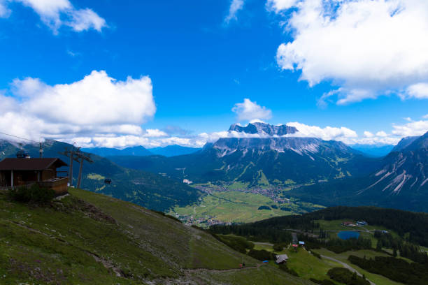 istock Panoramic drone view from Grubigstein, with rugged Zugspitze in background under blue sunny sky with cumulus clouds. Green valley at the foot of majestic alpine mountains, in Lermoos, Tyrol, 1337378792
