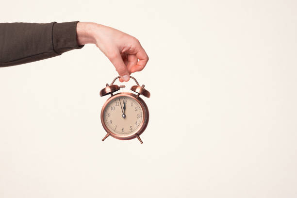 istock Male hand is holding an alarm clock over warm white background. 1337379988