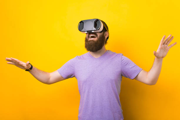 Bearded man is trying his VR headset in a studio over yellow background. stock photo