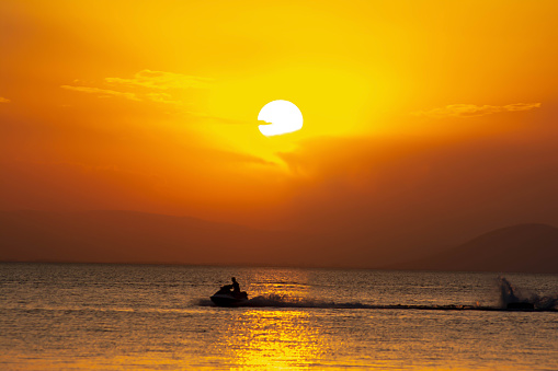 Jet ski and golden sun over the sea. Fantastic sunset over the sea. Tourist on a jet ski against the background of a golden sunset. Nice view, a man on a jet ski, the sea and the sunset.