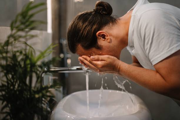 side view of young man washing his face in bathroom - gezicht wassen stockfoto's en -beelden