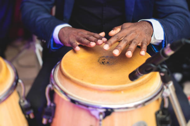 Bongo drummer percussionist performing on a stage with conga drums set kit during jazz rock show performance, with latin cuban band performing in the background, drummer point of view Bongo drummer percussionist performing on a stage with conga drums set kit during jazz rock show performance, with latin cuban band performing in background, drummer point of view drummer hands stock pictures, royalty-free photos & images