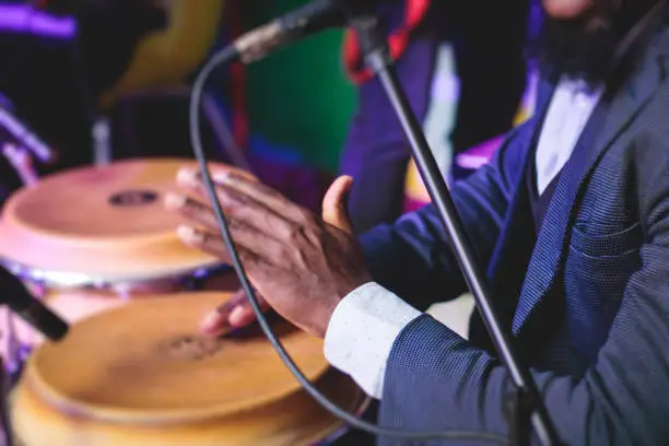 Bongo drummer percussionist performing on a stage with conga drums set kit during jazz rock show performance, with latin cuban band performing in background, drummer point of view