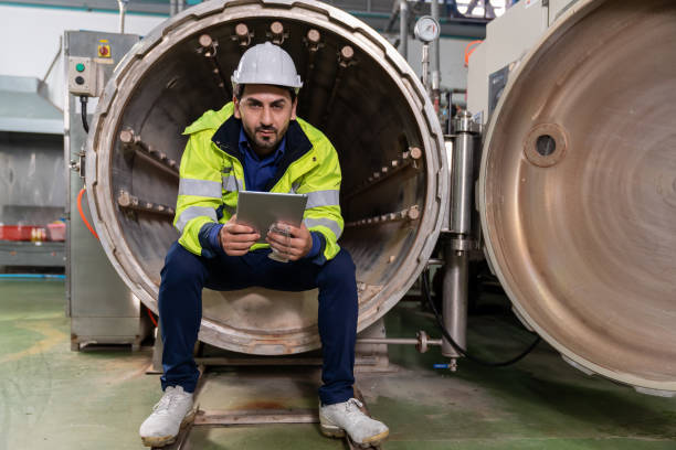 mecánico de fábrica masculino. ingeniero masculino que trabaja con tableta digital para reparar, mantener y verificar la caldera de vapor y los sistemas de control automático en la fábrica de bebidas. fábrica, concepto de industria - giant boilers fotografías e imágenes de stock