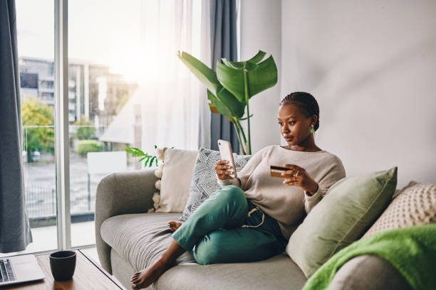 photo d’une jeune femme utilisant sa carte et son téléphone pour faire des achats en ligne à la maison - livraison à domicile photos et images de collection