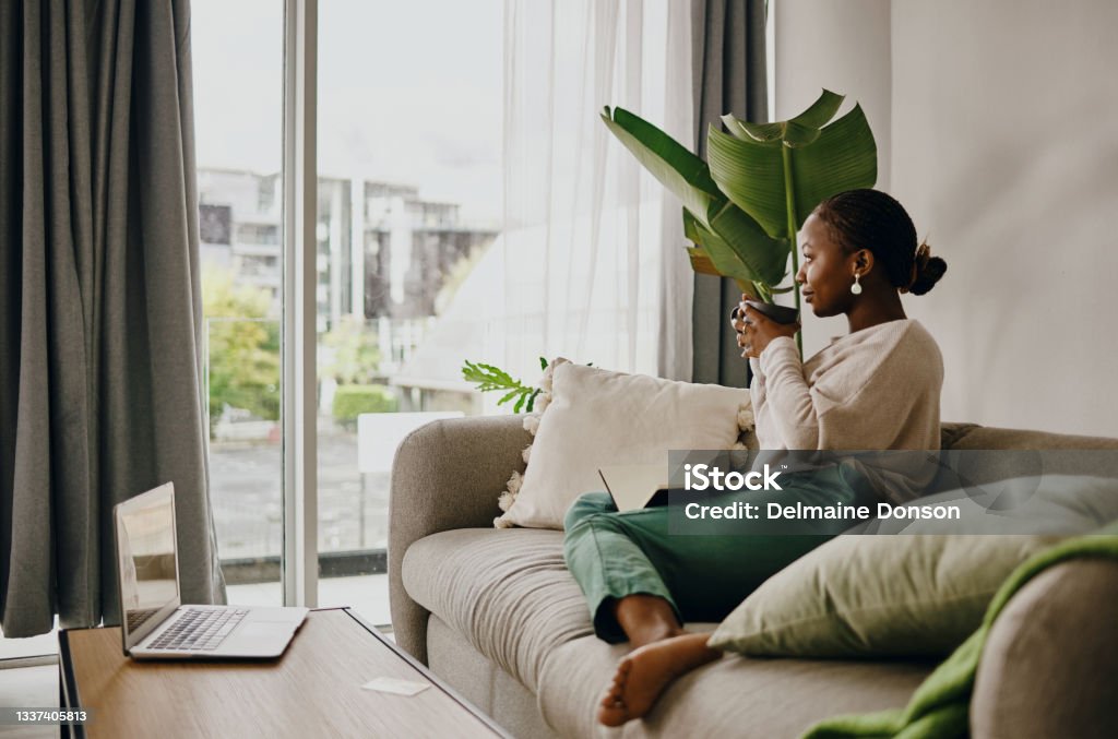 Shot of a young woman having coffee and relaxing at home One travels more usefully when alone because he reflects more Domestic Life Stock Photo