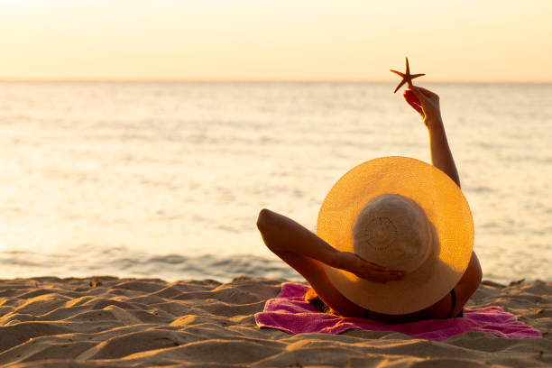young girl in a hat sunbathing on the beach at sunset