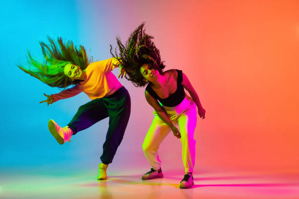 dos hermosas chicas de hip-hop bailando en el fondo naranja azul degradado en neón - dancing dancer hip hop jumping fotografías e imágenes de stock