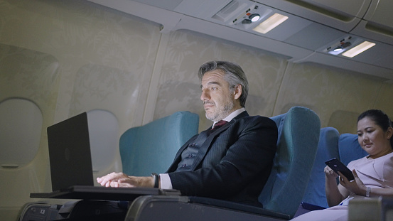 Mature businessman travelling in an airplane using his laptop.