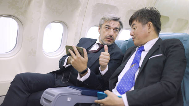 Businessmen using mobile phone in flight stock photo