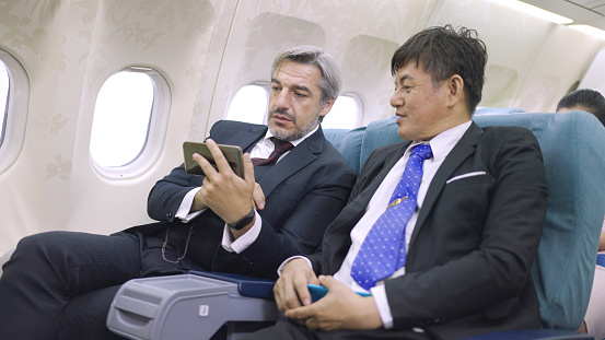 Two multi-ethnic businessmen having discussion on mobile phone while travelling in flight.