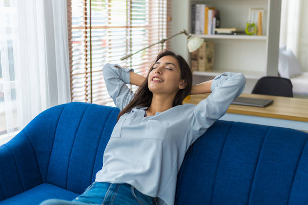 les femmes cacusiennes font une sieste pendant la journée pour reposer leurs yeux du travail acharné. femme se relaxant sur le canapé avec les yeux fermés et les mains derrière la tête à la maison. elle se tordit paresseusement et allongea une halei - exhaler photos et images de collection