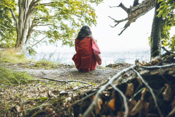 rear view on woman crouching on forest floor and looking down over baltic sea