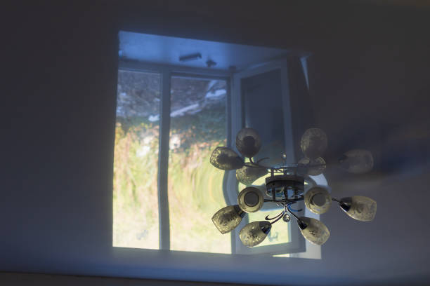 Off chandelier on a stretch white ceiling with the reflection of a light window in the darkness of the room. Background with copy space