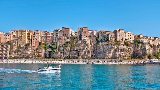 Tropea, Italy - June 18, 2021: View of Tropea with a beach and people from the Tyrrhenian Sea. In the foreground a speedboat with people.