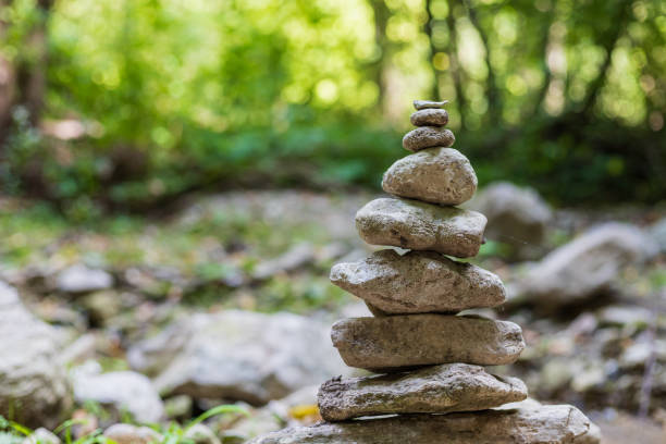 Stone cairn (oboo) adorned with ritual ribbons and prayer flags in a grassy mountain meadow surrounded by taiga forest, mountains, and blue sky in Altai Republic, Russia. This traditional spiritual site offers copy space for cultural, travel, and nature heritage concepts.
