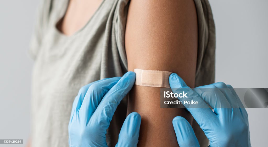 Medical healthcare worker putting bandage on the female arm after covid-19 vaccination Doctor putting plaster at female hand after injection of a corona virus vaccine. Corona virus protection, self care, healthy lifestyle, vaccination concept. Vaccination Stock Photo