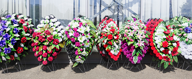 A row of wreaths for burial. The funeral wreaths are made of plastic flowers. Artificial wreaths for funerals. Exhibition sale.