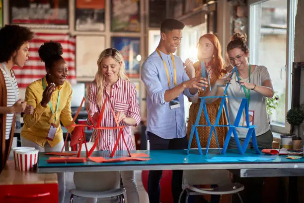 Photo of two group of employees making paper towers, separated in different competitive teams.