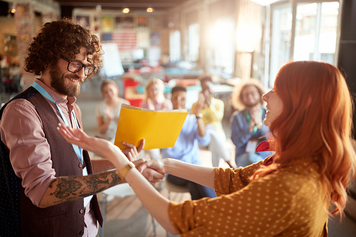 young redhead female congratulate to a caucasian business student after successful attending seminar, giving him certificate in folder. selective focus image.