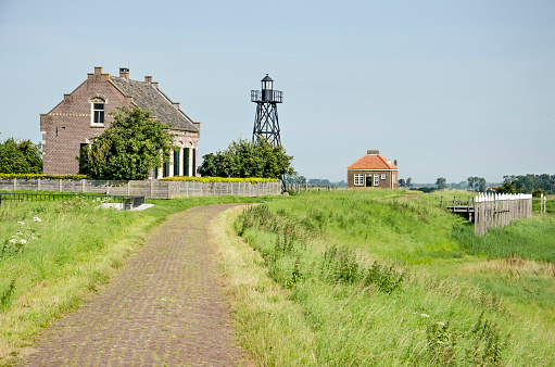 Schokland, The Netherlands, August 12, 2021: brick road leading up the northernmost moud of the former island, with some building, the lighthouse and the reconstructed harbour
