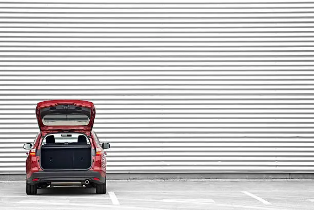 Red station wagon with trunk opened parked before a shopping mall wall