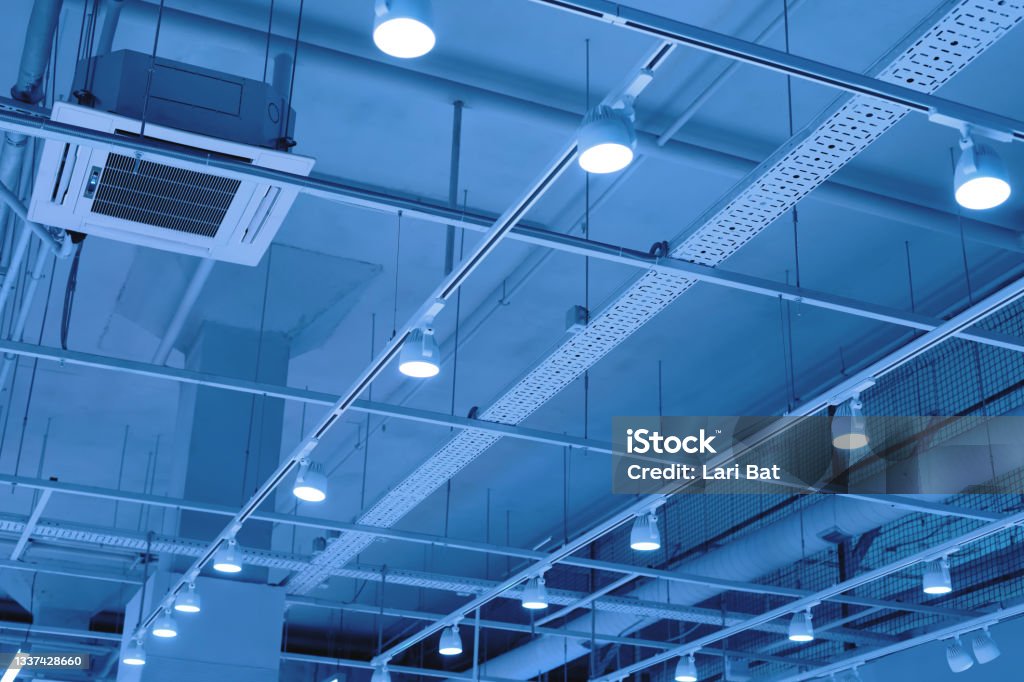 LED floodlights suspended from the ceiling on rails. lighting system in a shopping center, warehouse or office. Ceiling with bright lights in a modern commercial real estate object. Ceiling with bright lights in a modern warehouse, shopping center building, office or other commercial real estate object. Directional LED lights on rails under the ceiling. Tinted. LED Light Stock Photo