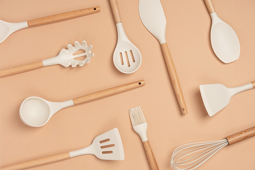 Pattern made from cooking utensil set. Silicone kitchen tools with wooden handle on beige background. Top view Flat lay