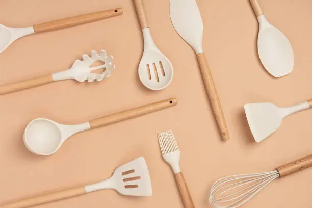 Pattern made from cooking utensil set. Silicone kitchen tools with wooden handle on beige background. Top view Flat lay.