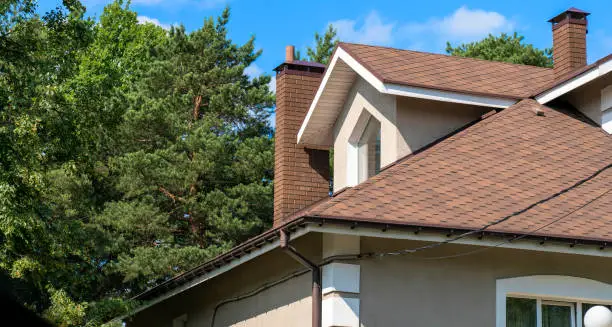 Photo of Close-up of asphalt shingled roofing construction with chimney, plastic soffit, fascia board and roof gutters installed