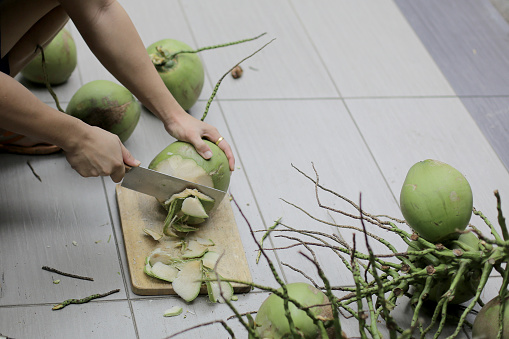 An Asian young man is attempting to cut open coconut fruit at home.