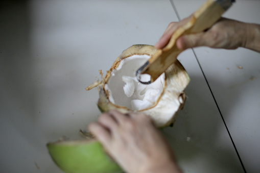 An Asian young man is attempting to grate coconut flesh at home.