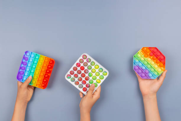 istock Many hands holding pop it fidget toys on blue background. Push pop-it fidgeting game helps relieve stress, anxiety 1337433159