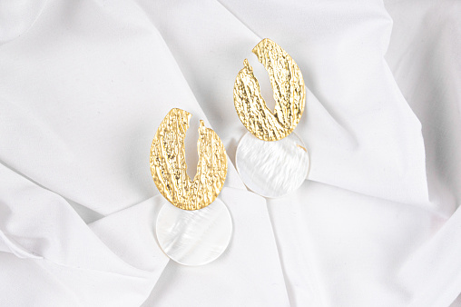 Pair of beautiful gold earrings with pendants made of nacre on white fabric backgrund. High quality photo