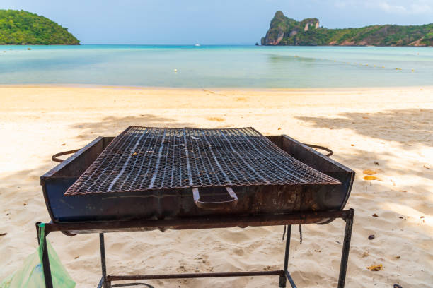 old and empty outdoor barbecue grill meat roaster with sea sunlight and beach in background. - bonfire beach fire barbecue imagens e fotografias de stock