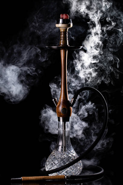 Hookah shisha with glass flask and clay bowl with white smoke on a black background. Traditional Eastern relaxation stock photo