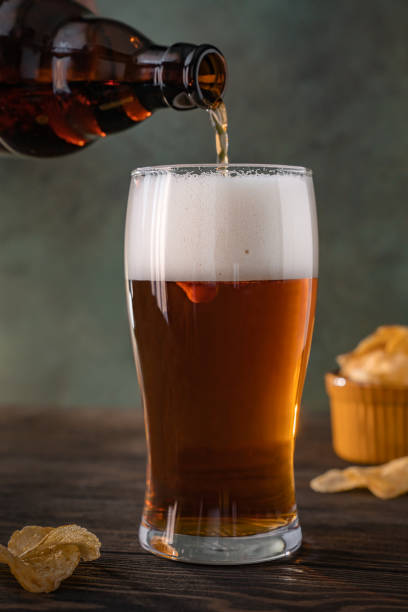 istock Pouring fresh beer from brown bottle into glass on dark background 1337438402