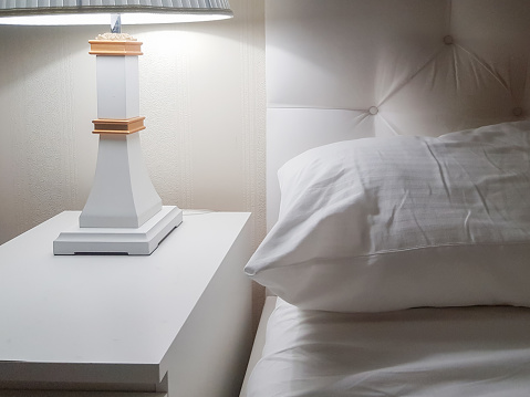 Luxury modern design of a bright bedroom with a bedside table and a night light and a pillow on the bed, preparing for bed.