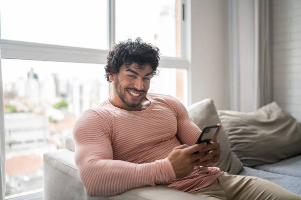 istock Portrait of a happy young man using smartphone at home 1337447961