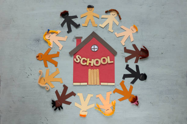 Multi-ethnic paper dolls boys and girls claiming for equal access to school. Children's rights, human's rights. Human diverse paper chain around a cardboard school on a blue background childrens rights stock pictures, royalty-free photos & images