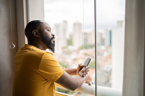 Man contemplating and holding mobile phone at home