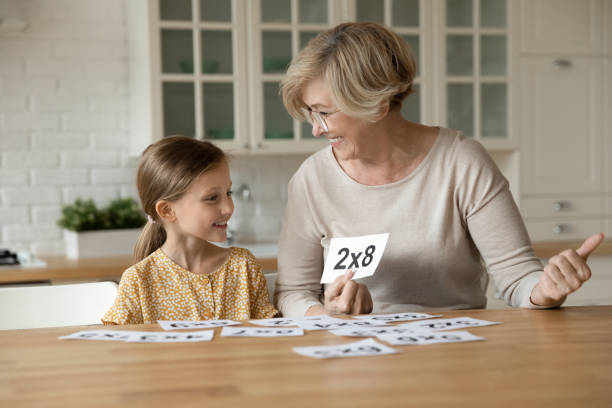 smiling mature grandmother with little granddaughter learning multiplication table - happy kid flash imagens e fotografias de stock