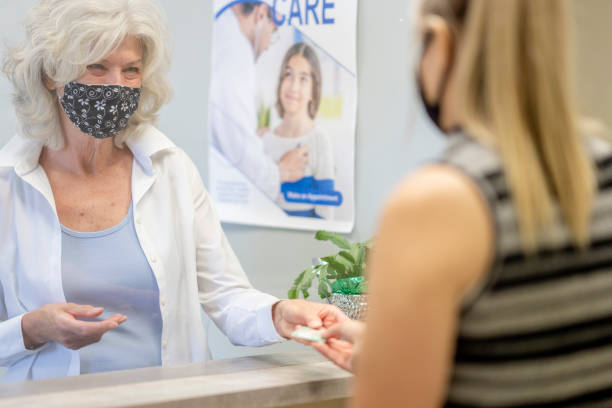 mujer mayor enmascarada en una clínica médica - healthcare and medicine receptionist paying credit card fotografías e imágenes de stock