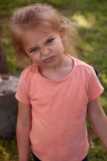 portrait d’une petite fille fronçant les sourcils regardant l’appareil photo dans la cour arrière - beautiful lifestyles human face blond hair photos et images de collection