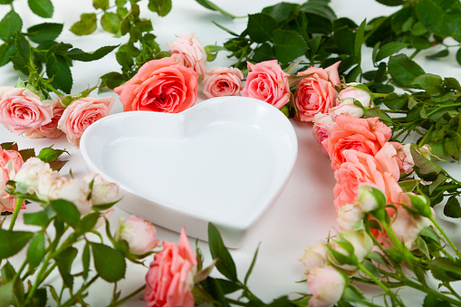 Bouquet of pink roses and a plate in the form of a heart on a light background. Greeting card.