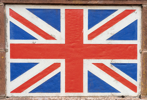 A close-up of a Union Jack flag, an old weathered painted surface on stone.