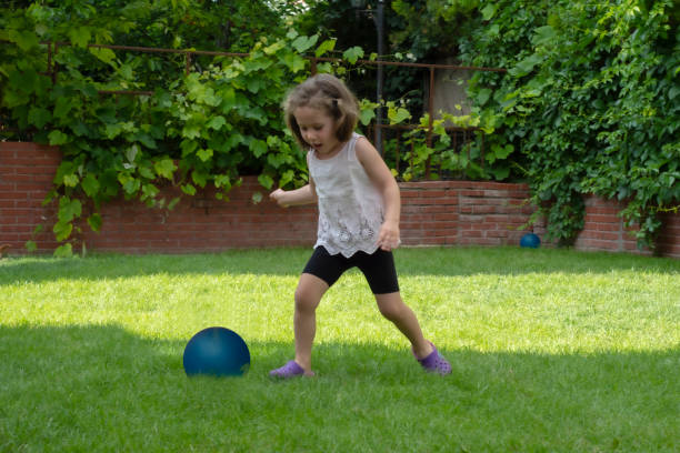 Little girl is playing with her blue ball in the garden of their house. Selective Focus Girl